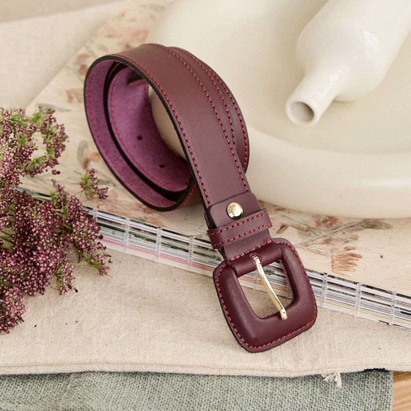 Burgundy leather women's belt with covered buckle, coiled behind a vase - MONPIEL