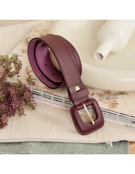 Women’s burgundy leather belt with covered buckle, coiled behind a vase - MONPIEL Women’s burgundy leather belt with covered buckle, coiled behind a vase - MONPIEL