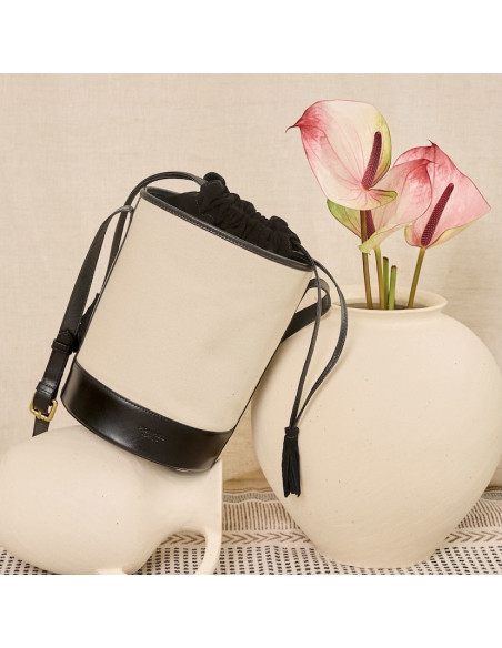 Black leather canvas bucket bag, front view, tilted, resting on a vase - MONPIEL Black leather canvas bucket bag, front view, tilted, resting on a vase - MONPIEL