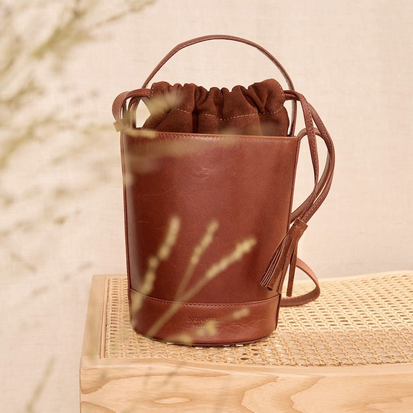 Small Havana leather round cube bag, front view, resting on a bench - MONPIEL