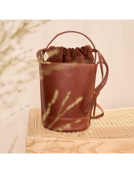 Small round cube leather bag in Havana color, front view, resting on a bench - MONPIEL