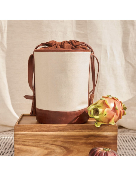 Bolsa cubo em canvas e couro em tom couro, vista frontal apoiada em madeira com cortina ao fundo - MONPIEL