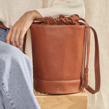 Sac rond en forme de seau de couleur havane, vue de face posé sur un meuble, avec un miroir en arrière-plan - MONPIEL 2