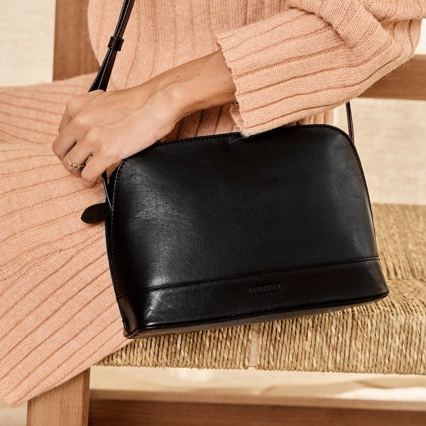 Medium black leather bag, front view, hanging from the shoulder on top of a chair - MONPIEL