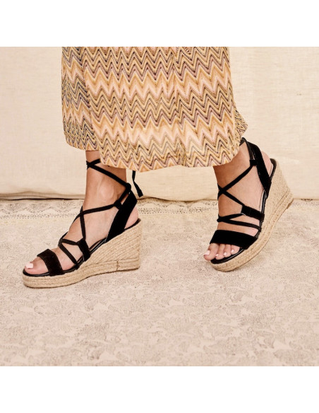 Black leather strap wedge espadrille, profile view, walking on carpet - MONPIEL Black leather strap wedge espadrille, profile view, walking on carpet - MONPIEL