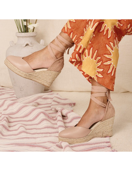 Espadrille em couro com cunha Elba em tom nude, vista lateral com pernas cruzadas sobre tapete - MONPIEL Espadrille em couro com cunha Elba em tom nude, vista lateral com pernas cruzadas sobre tapete - MONPIEL