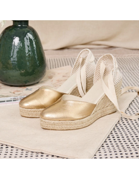 Espadrille em couro com cunha Elba em tom dourado, vista em perspectiva com vaso ao fundo - MONPIEL Espadrille em couro com cunha Elba em tom dourado, vista em perspectiva com vaso ao fundo - MONPIEL