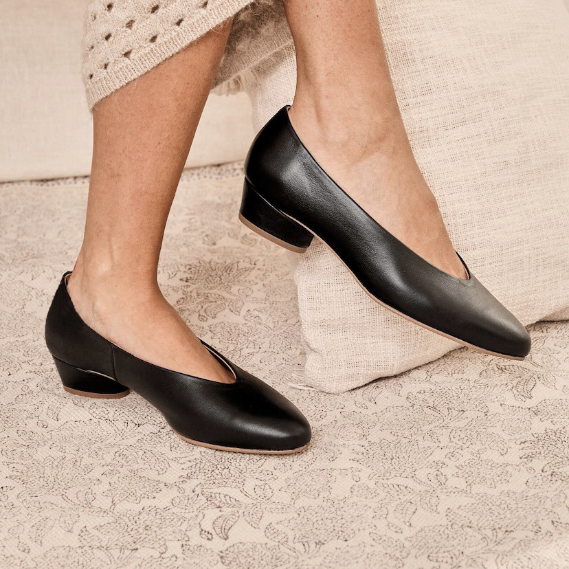 Black heeled ballerina, side view, legs crossed in front of a cushion - MONPIEL