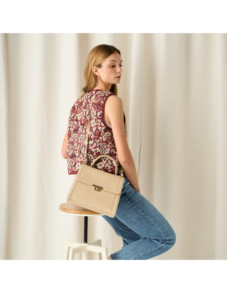 Sac femme en cuir des années 60 couleur beige, vue de face porté à l'épaule, plan moyen du mannequin assis sur un tabo - MONPIEL