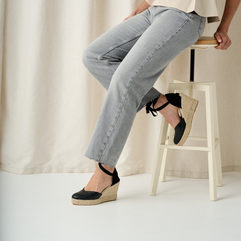 Elba leather wedge espadrille in black, toe resting on stool, side view, medium shot - MONPIEL