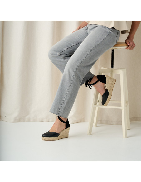 Elba Keilabsatz-Espadrille aus schwarzem Leder, mit der Spitze auf einem Hocker gestützt, Seitenansicht, Nahaufnahme - MONPIEL Elba Keilabsatz-Espadrille aus schwarzem Leder, mit der Spitze auf einem Hocker gestützt, Seitenansicht, Nahaufnahme - MONPIEL
