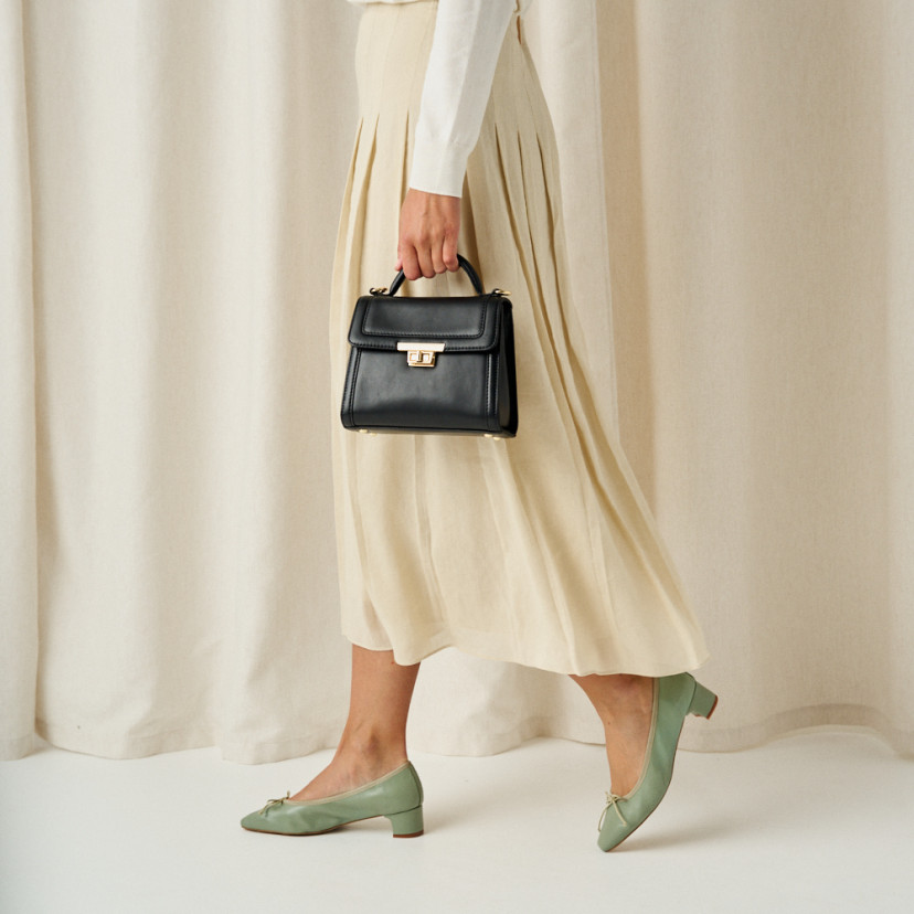 Bolsa de couro pequena estilo 60's para mulheres na cor preta, plano médio com modelo de perfil, detalhes dos passos d - MONPIEL