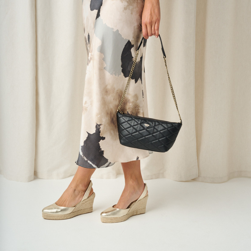 Platinum leather wedge espadrille with crossed legs standing and detail of leather bag in hand - MONPIEL