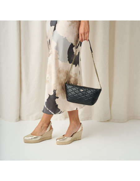 Platinum-colored leather wedge espadrille with crossed legs, standing, and detail of leather bag in hand - MONPIEL Platinum-colored leather wedge espadrille with crossed legs, standing, and detail of leather bag in hand - MONPIEL