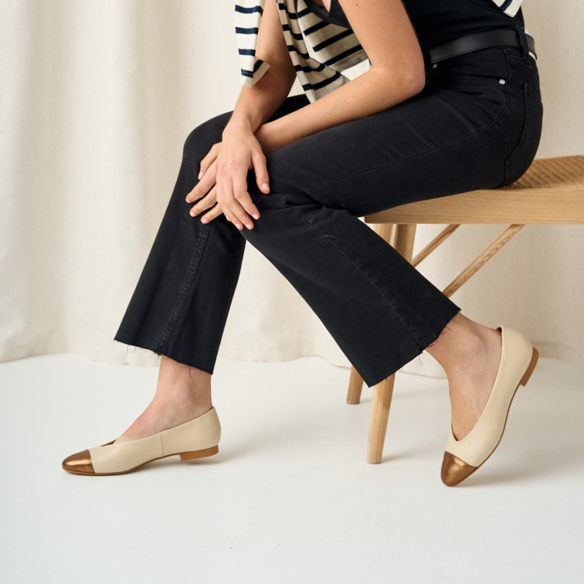 Ameliè flat ballerina with metallic beige/copper toe cap, side view with legs open, model sitting on the bench - MONPIEL