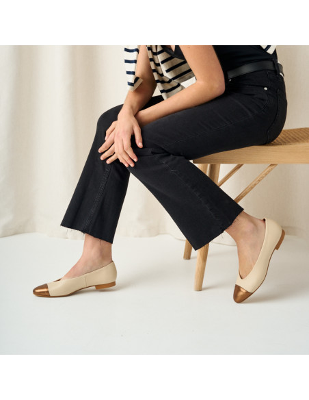 Ameliè flat ballerina with metallic beige/copper toe cap, side view with legs apart, model sitting on the bench - MONPIEL Ameliè flat ballerina with metallic beige/copper toe cap, side view with legs apart, model sitting on the bench - MONPIEL