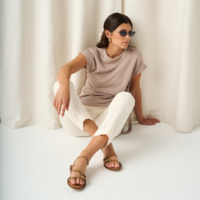 Amalfi buckle sandal in leather colour, full shot of the model sitting on the floor with crossed feet and sunglasses - MONPIEL