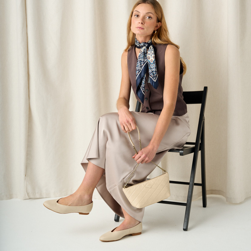 Women's small quilted leather bag New York in beige with perspective view, full shot of the model sitting on the chair - MONPIEL
