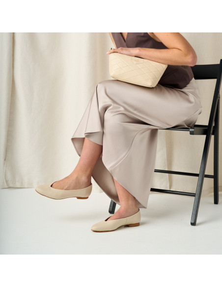 Ballerina plana na cor bege com plano médio e modelo com pernas cruzadas sentada na cadeira de perfil - MONPIEL Ballerina plana na cor bege com plano médio e modelo com pernas cruzadas sentada na cadeira de perfil - MONPIEL