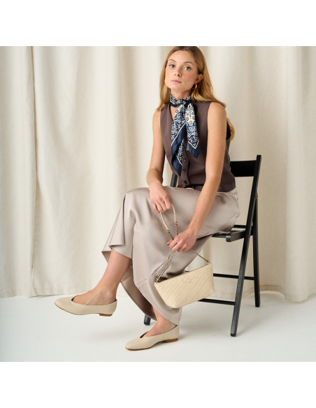 Flat slipper in beige with model in full shot sitting on chair - MONPIEL Flat slipper in beige with model in full shot sitting on chair - MONPIEL