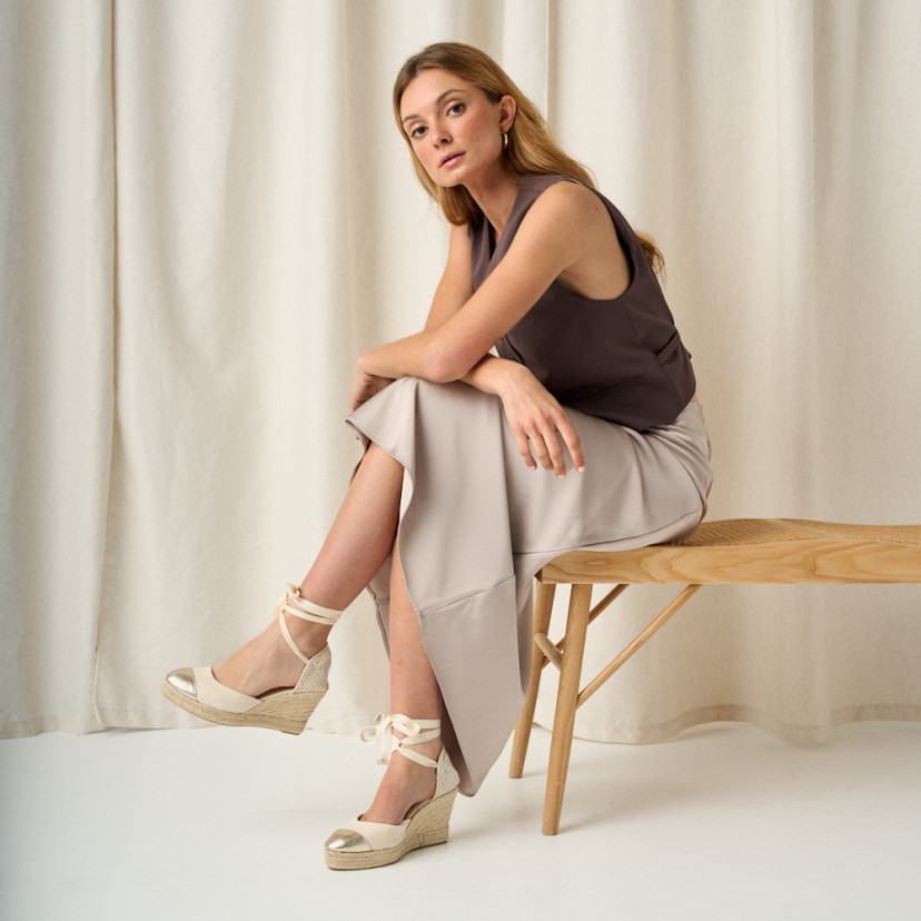 Leather wedge espadrille with toe cap in platinum with crossed legs, full shot of the model sitting on the bench - MONPIEL
