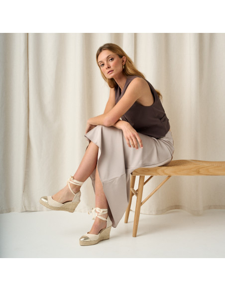 Espadrilla con zeppa in pelle con punta color platino e gambe incrociate, piano generale del modello seduto sulla panc - MONPIEL Espadrilla con zeppa in pelle con punta color platino e gambe incrociate, piano generale del modello seduto sulla panc - MONPIEL