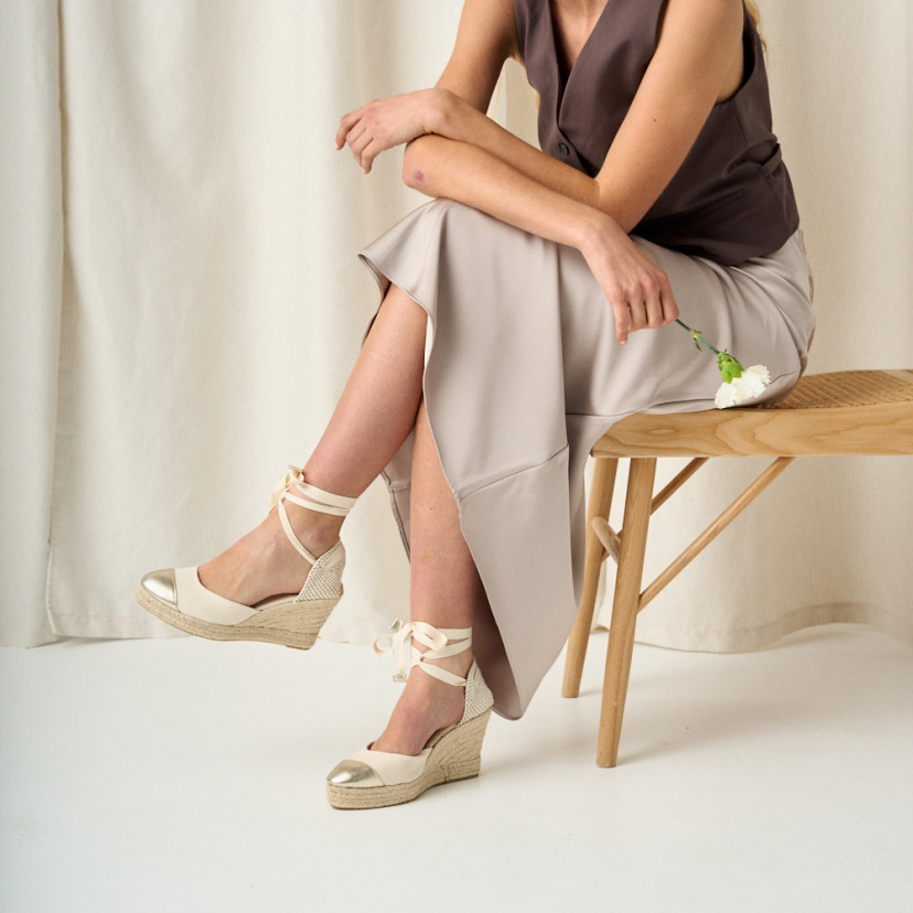 Leather wedge espadrille with toe cap in platinum with crossed legs and flower in hand, medium shot - MONPIEL