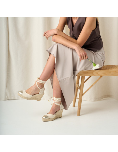 Espadrille compensée en cuir avec bout pointu en couleur platine, jambes croisées et fleur à la main, plan moyen - MONPIEL Espadrille compensée en cuir avec bout pointu en couleur platine, jambes croisées et fleur à la main, plan moyen - MONPIEL