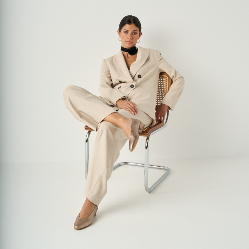 Heeled flat slipper in cappuccino bronze with full shot of the model sitting on the chair, perspective view - MONPIEL