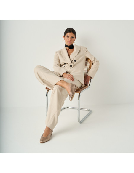 Heeled flat slipper in cappuccino bronze with full shot of the model sitting on the chair, perspective view - MONPIEL Heeled flat slipper in cappuccino bronze with full shot of the model sitting on the chair, perspective view - MONPIEL