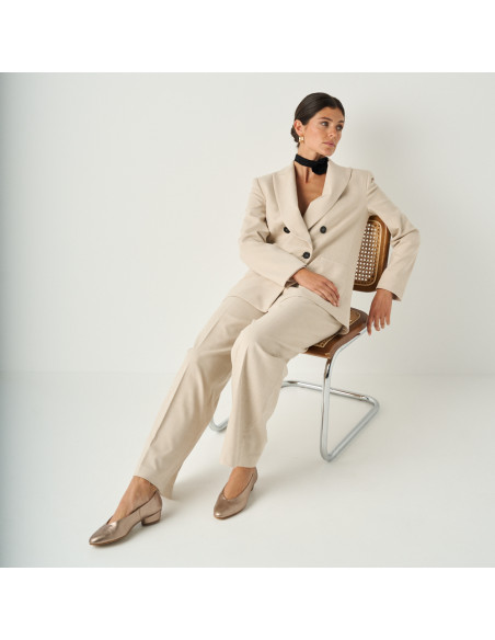 Bronze cappuccino-colored ballet flat with a heel, general shot of the model sitting on the chair, perspective view - MONPIEL Bronze cappuccino-colored ballet flat with a heel, general shot of the model sitting on the chair, perspective view - MONPIEL
