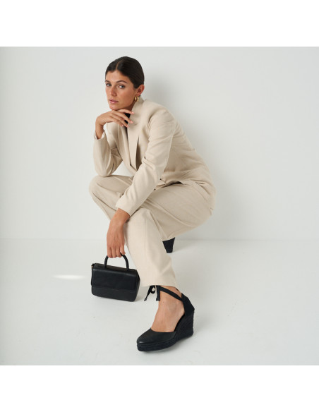 Espadrille compensée Creta en cuir noir dans un plan général du modèle accroupi avec une jambe tendue et un sac en cui - MONPIEL