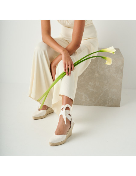 Espadrille Elba en soie pour mariée couleur blanche, vue en perspective d'en haut, tenant une fleur à la main - MONPIEL