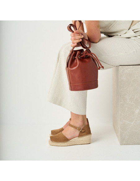 Mink-colored media Menorca wedge espadrille with a profile view, model sitting on a marble cube holding a leather bag - MONPIEL