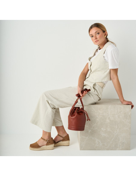 Espadrille à talon compensé média Menorca couleur vison, vue de profil, modèle assis sur un cube en marbre, plan génér - MONPIEL