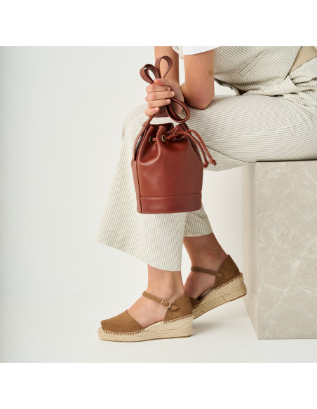 Small leather bombonera sack bag in leather color, held by the handle with a profile view and espadrille detail - MONPIEL Small leather bombonera sack bag in leather color, held by the handle with a profile view and espadrille detail - MONPIEL