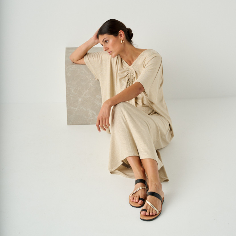 Mykonos leather Greek sandal in black, model sitting on the floor leaning on a marble cube - MONPIEL