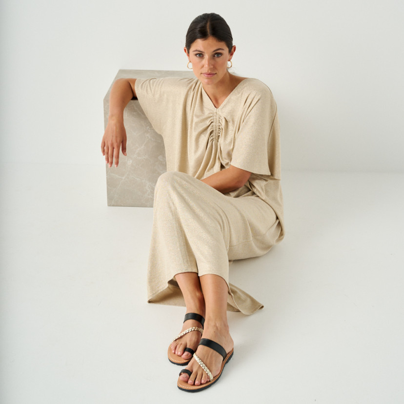 Sandália grega de couro Mykonos na cor preta, modelo sentada no chão apoiada em cubo de mármore, vista em perspectiva - MONPIEL