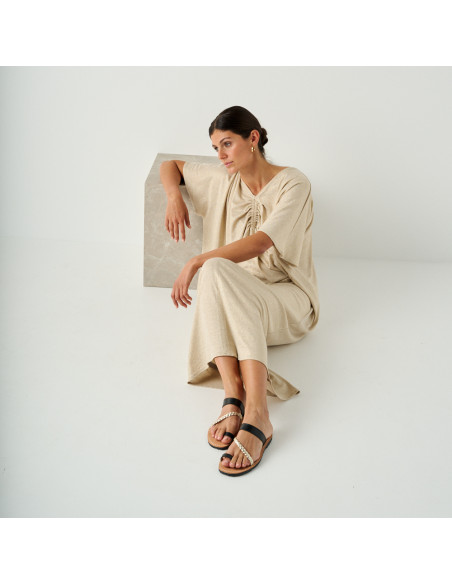 Sandalo greco in pelle Mykonos nero, modella seduta a terra appoggiata a un cubo di marmo, vista prospettica - MONPIEL Sandalo greco in pelle Mykonos nero, modella seduta a terra appoggiata a un cubo di marmo, vista prospettica - MONPIEL