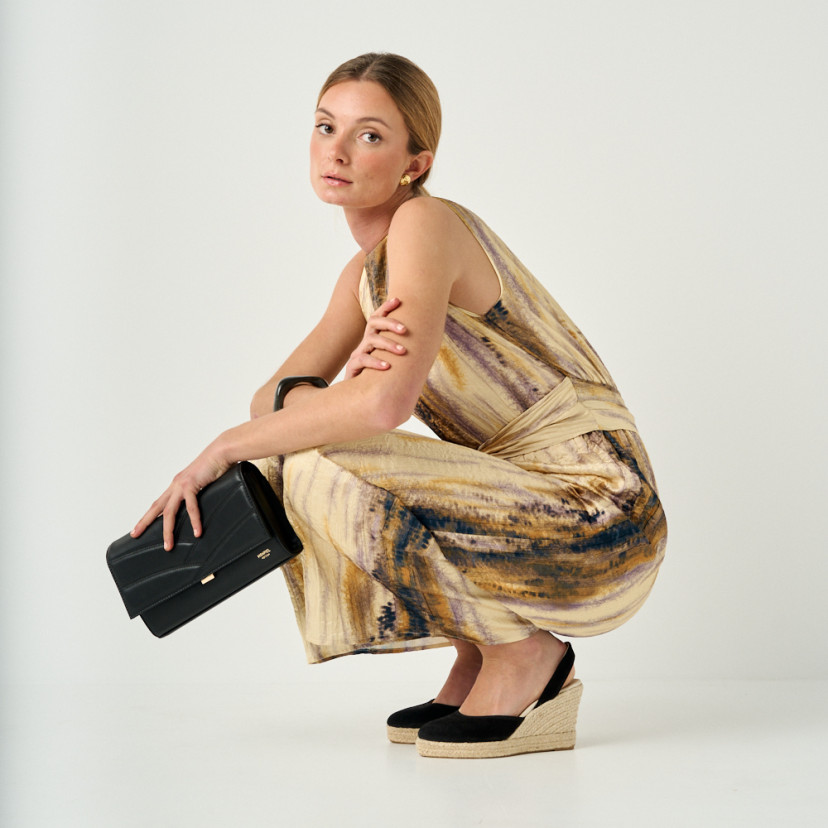 Venice black leather women's handheld purse, held in hand with model crouching in full shot - MONPIEL
