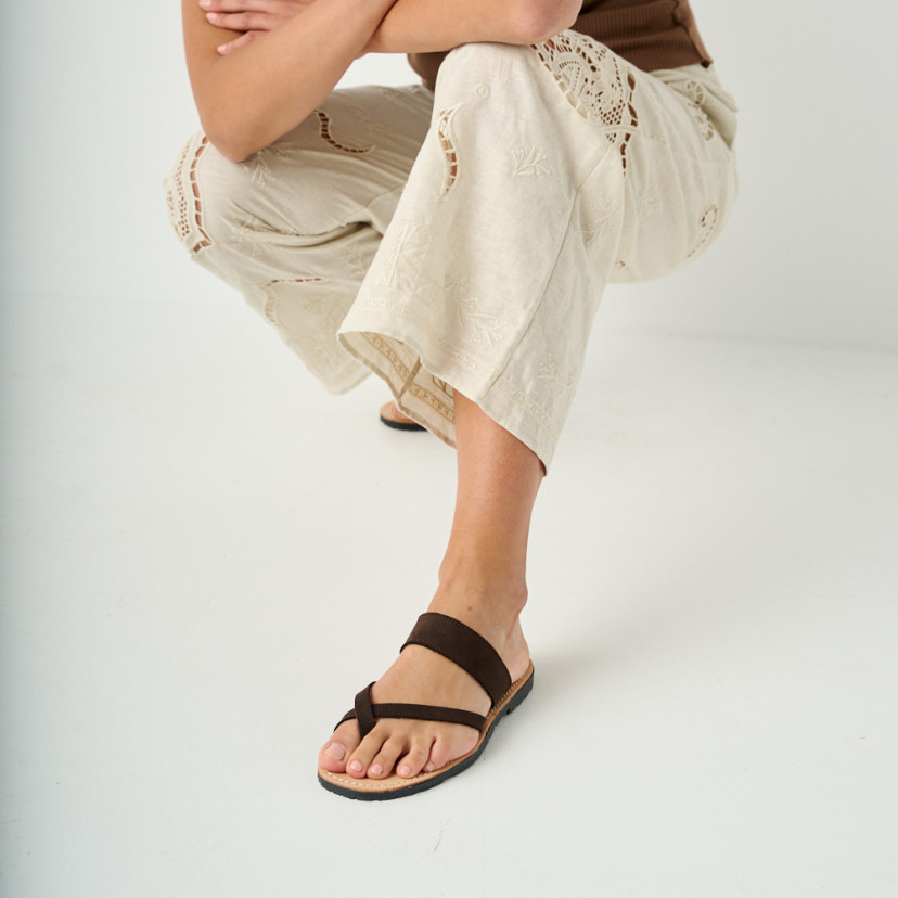 Santorini brown leather Greek sandal with perspective view, leg forward, model crouching - MONPIEL