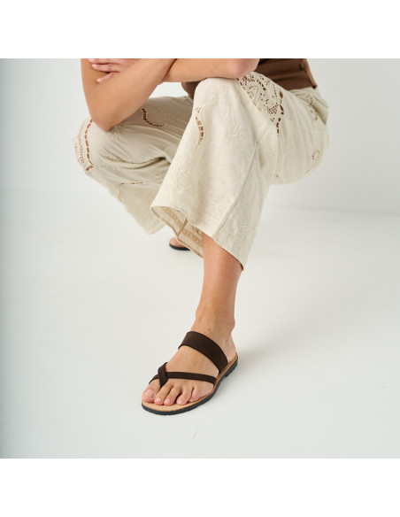 Santorini brown leather Greek sandal with perspective view, leg forward, model crouching - MONPIEL