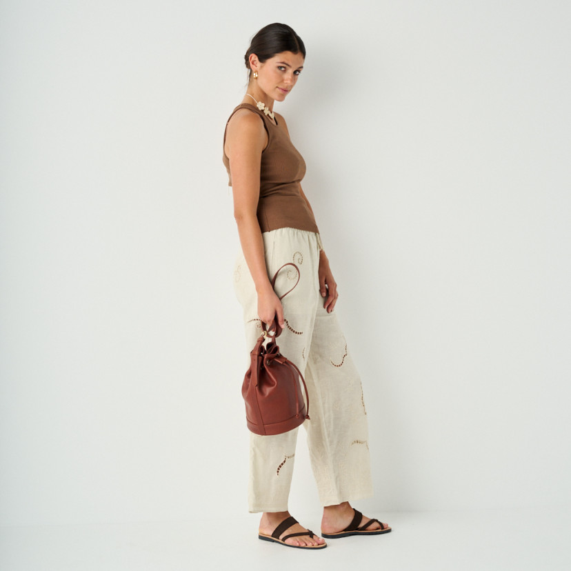 Santorini brown leather Greek sandal with perspective view, model in profile in full shot with leather handbag in hand - MONPIEL