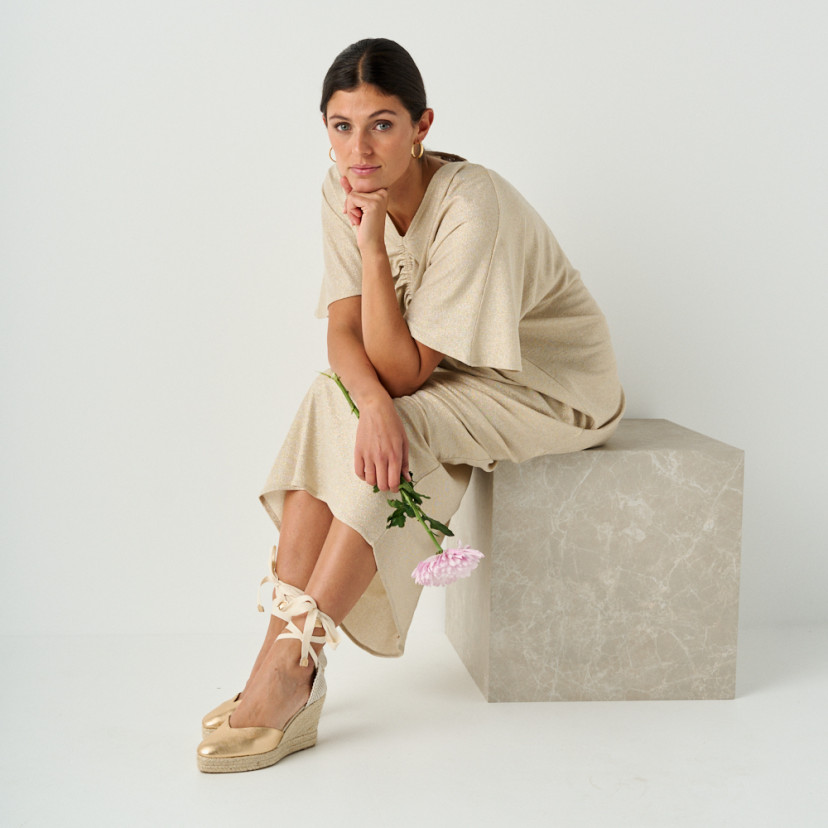 Elba gold leather wedge espadrille with perspective view, model sitting on marble cube, full shot - MONPIEL