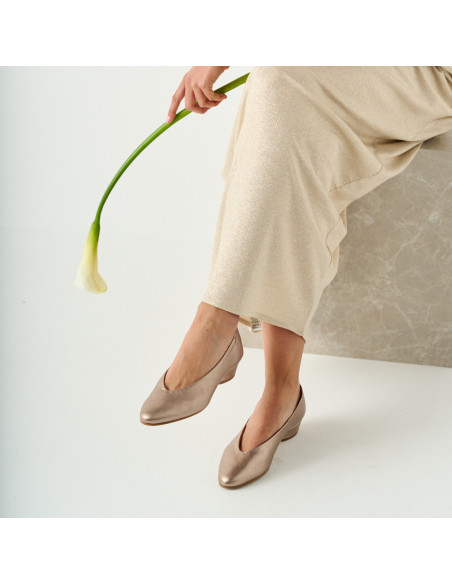 Ballerine à talon couleur cappuccino bronze avec une fleur à la main et les jambes croisées, assise sur un cube en mar - MONPIEL Ballerine à talon couleur cappuccino bronze avec une fleur à la main et les jambes croisées, assise sur un cube en mar - MONPIEL