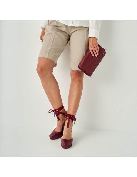 Keil-Espadrille Creta aus Leder in Bordeaux, Halbnahaufnahme mit Lederclutch in der Hand - MONPIEL