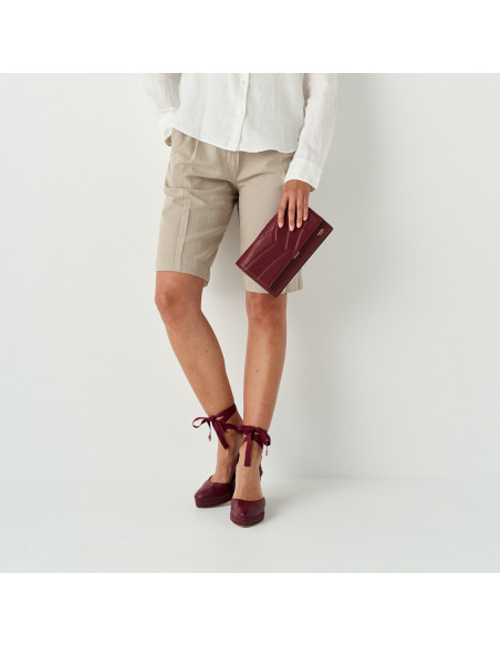 Venice women’s leather clutch bag in burgundy held in hand with detail of burgundy wedges - MONPIEL