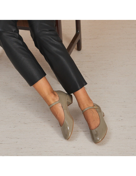 Sapato feminino tipo Mary Jane de couro envernizado na cor taupe com pernas esticadas, modelo sentada na cadeira - MONPIEL Sapato feminino tipo Mary Jane de couro envernizado na cor taupe com pernas esticadas, modelo sentada na cadeira - MONPIEL