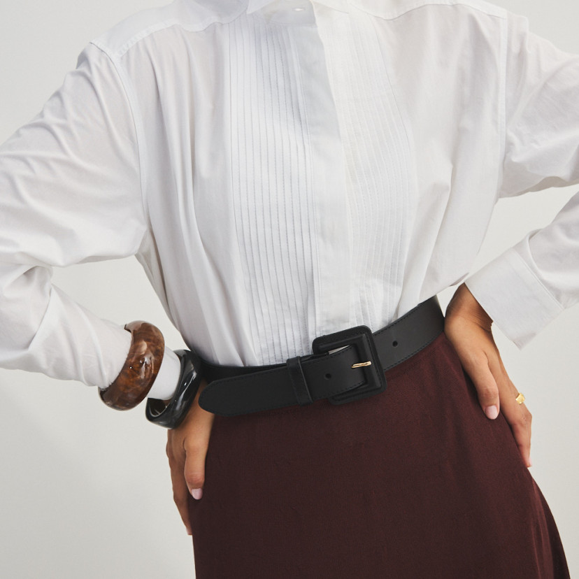 Wide women's leather belt with covered buckle in black, over burgundy skirt and white shirt, front view - MONPIEL