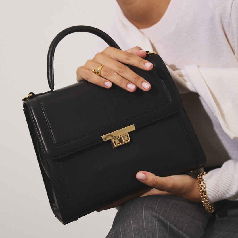 Bolsa de couro feminina anos 60 na cor preta com vista frontal, segurada com as duas mãos em close-up - MONPIEL